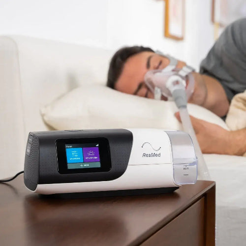 ResMed CPAP machine on a nightstand with a person using it in the background.