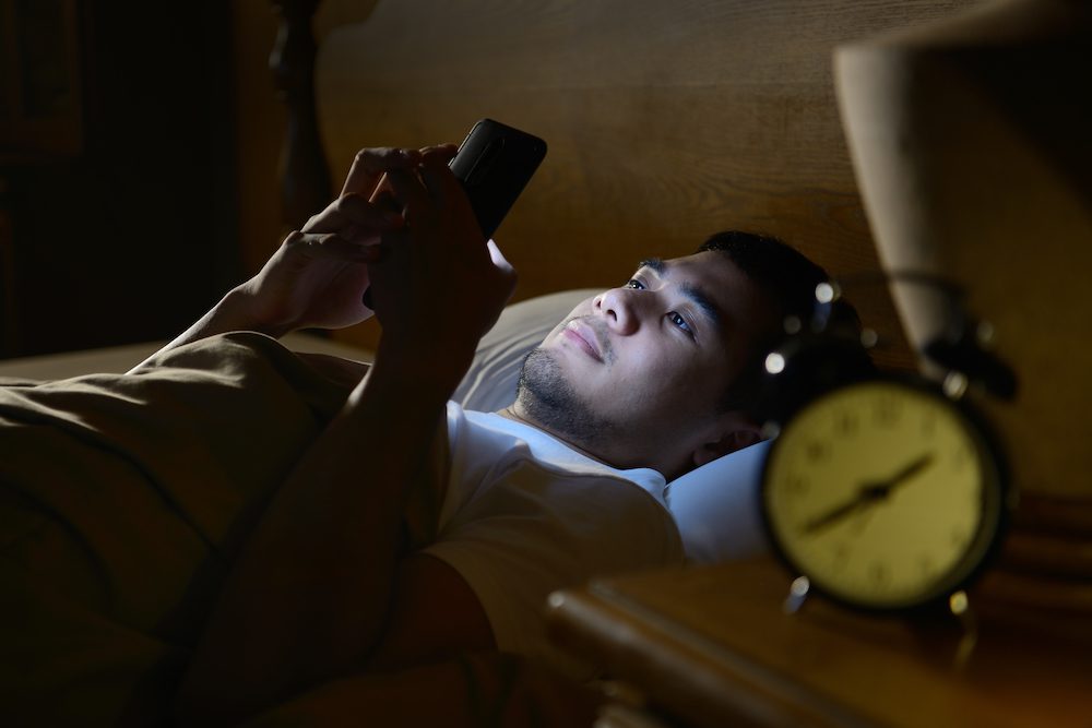 stock photo of a young man using phone in bed