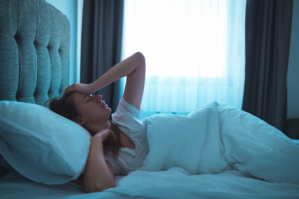 A stock photo of a young woman lying in bed at night, wide awake
