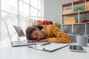 a young professional woman rests with her head on her desk in an office